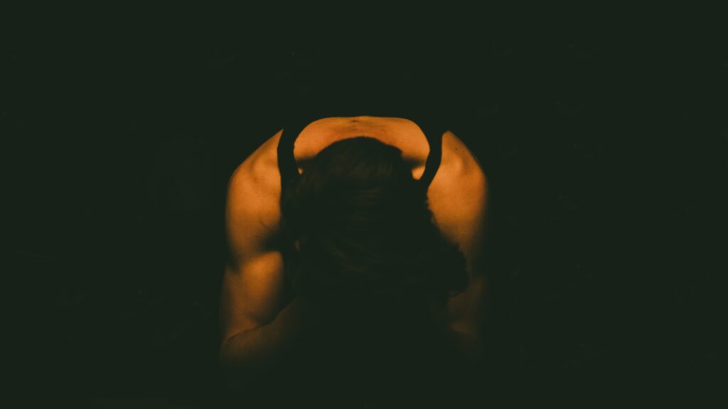 Photo of a man holding his head in his hands in a dark room.