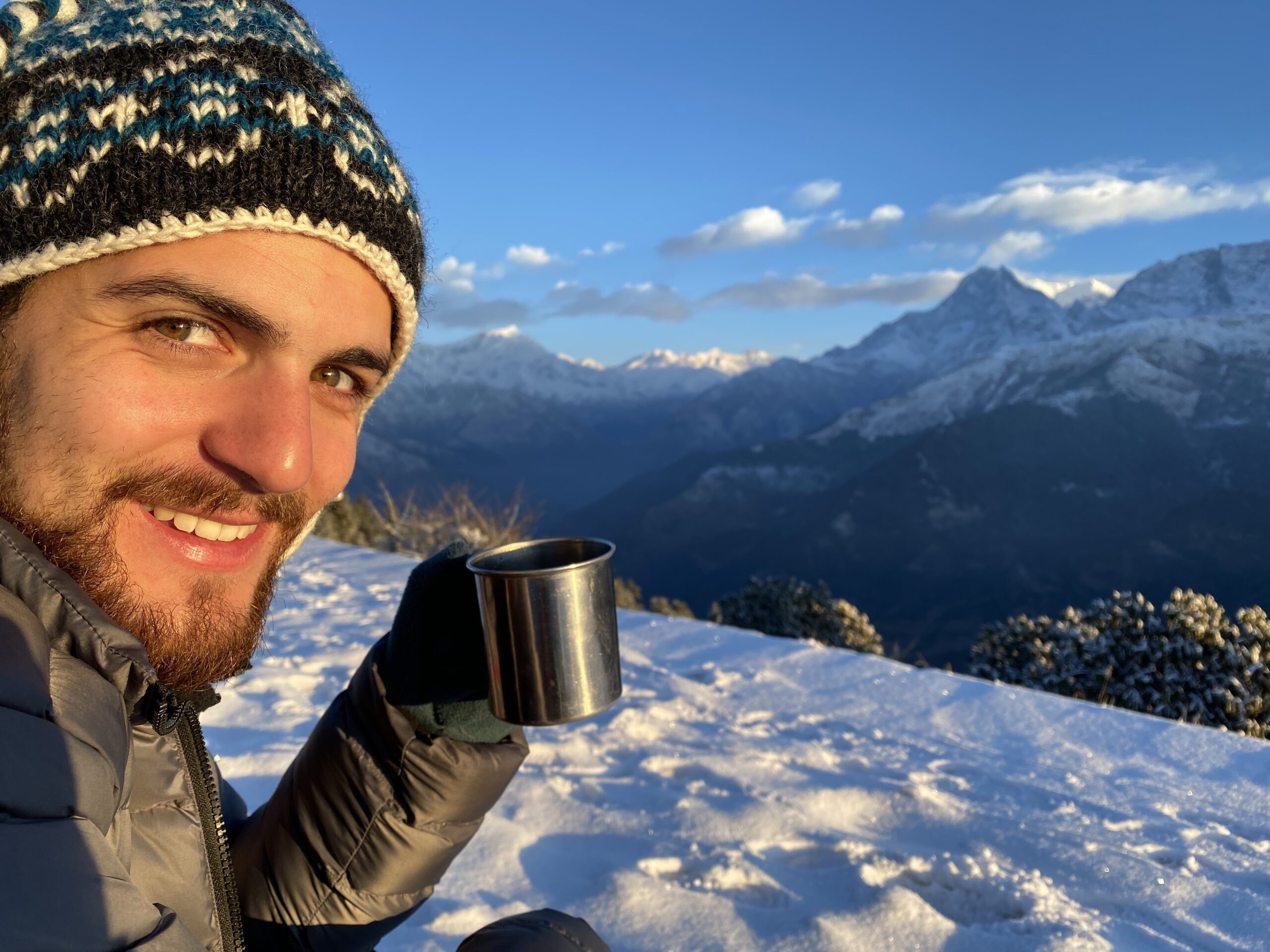 Photo of Oliver Page sitting in front of the Himalayas with a mug of tea